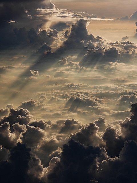 an aerial view of a dramatic cloudscape with layers of clouds illuminated by sunlight. light rays pierce through the cloud cover, creating a striking contrast of light and shadow. the scene evokes a sense of awe and wonder.