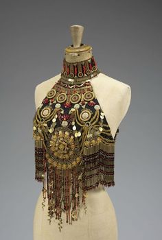 an image of a mannequin wearing a beautiful ornate beaded costume jewelry piece,  the jewelry has gold and silver beads, red beads, and a black base with tassels and fringe.