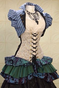 a steampunkinspired dress is displayed on a mannequin. the dress features a white corset with black lacing, a blue and white striped jacket, a creamcolored blouse, and a layered skirt with blue, green, and black fabric.