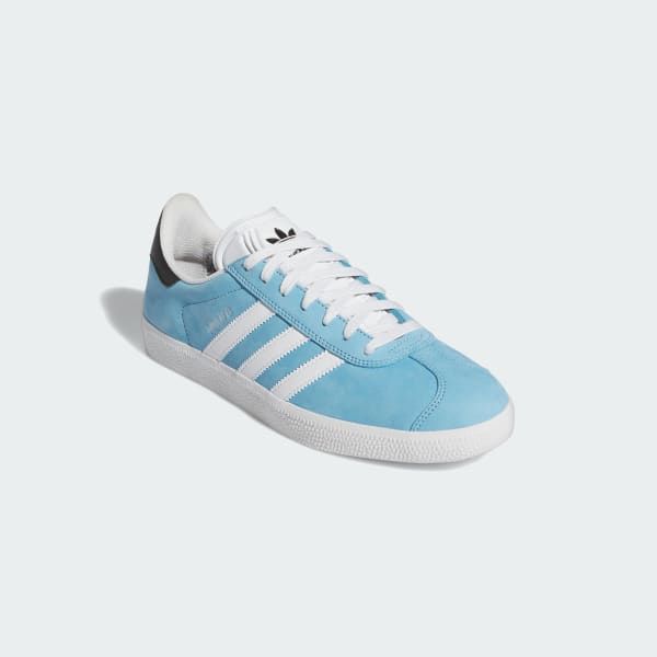 a pair of light blue adidas gazelle shoes with white stripes and black trim.  the shoes are on a white background.