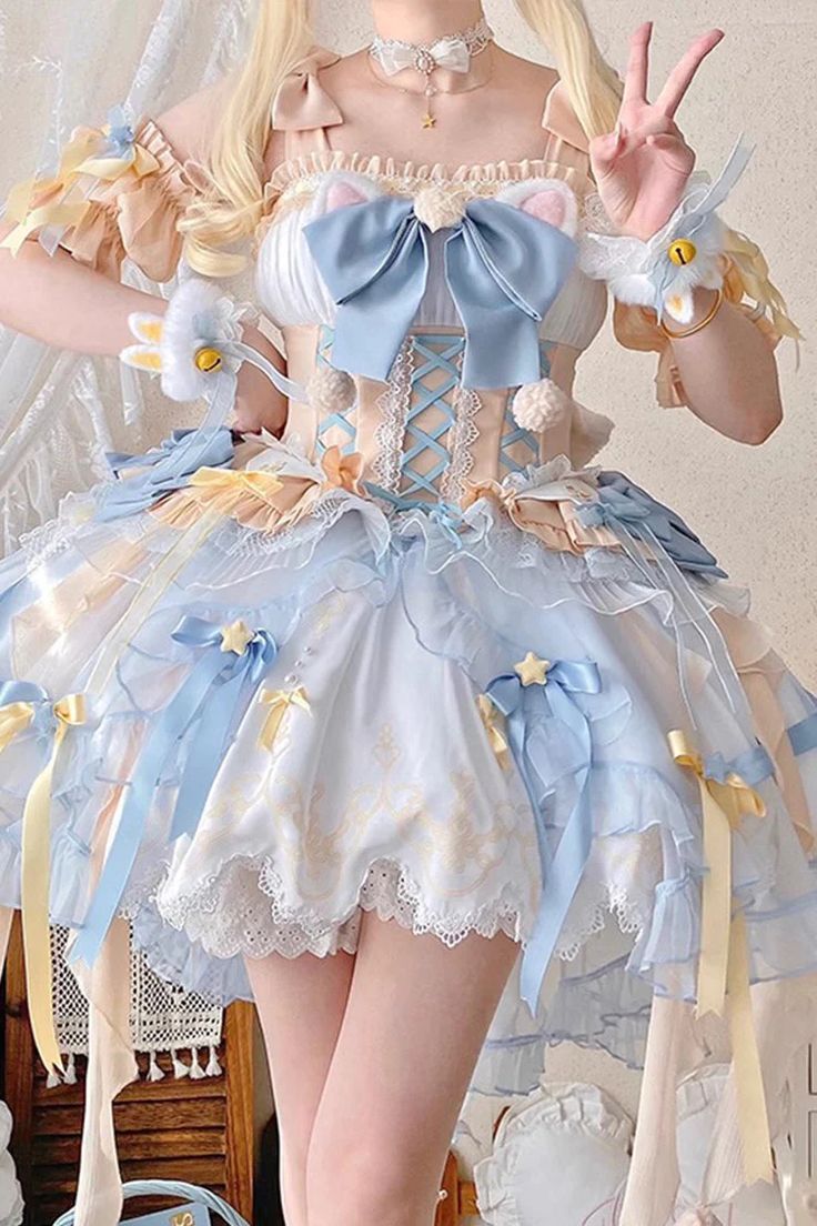 a young woman is posing for a picture in a frilly lolita dress. the dress is predominantly light blue and white with yellow accents, and features a lace trim, bows, and star patterns. the bodice of the dress is corseted and has a large blue bow in the center. she is also wearing white gloves with fluffy white cat ears attached.  the background is blurred and appears to be a room with a wooden floor.