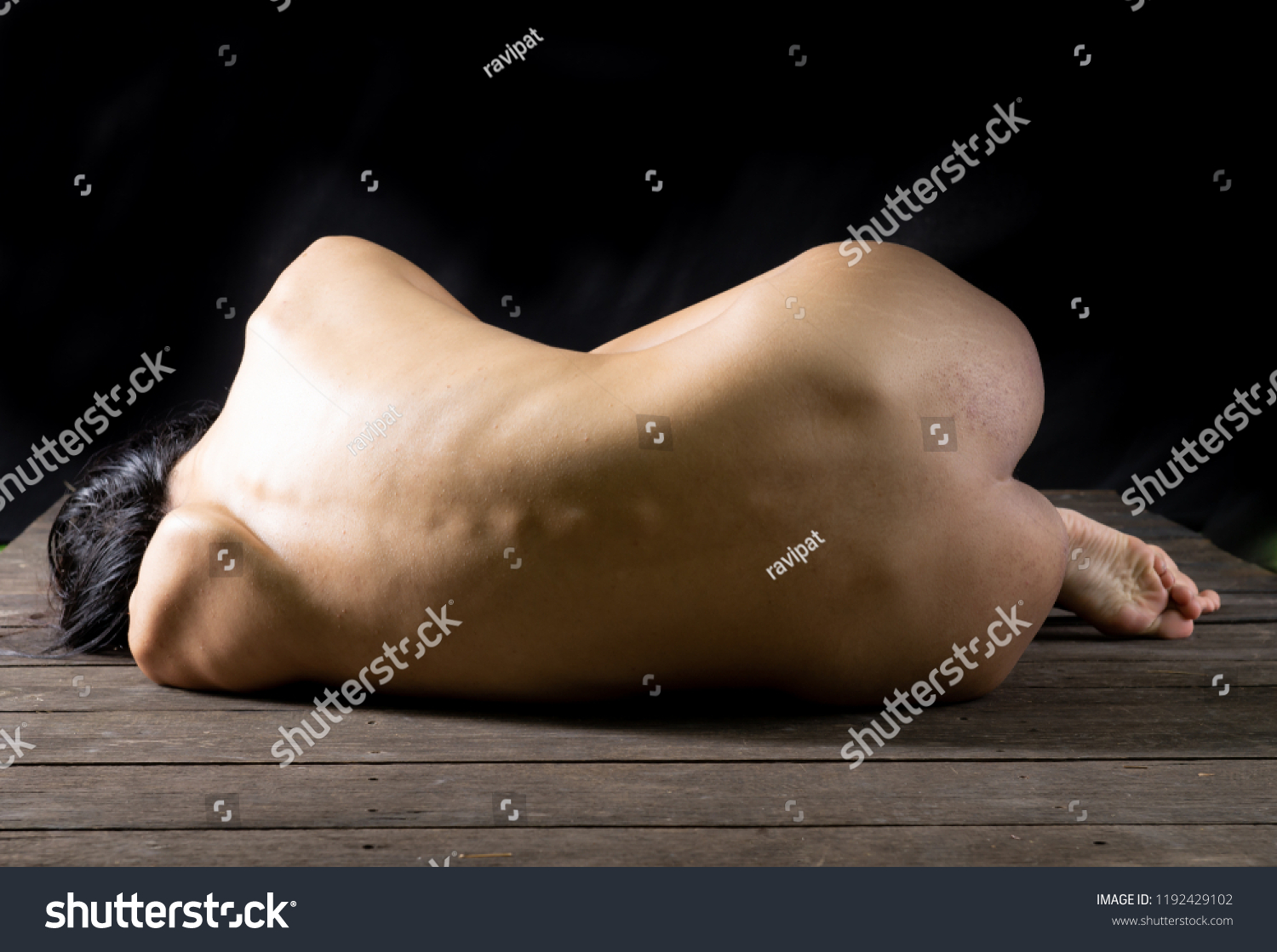 a nude person lays on their front with their back facing up on a wooden surface.