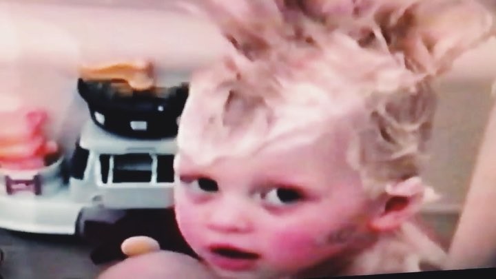 a child with soapy hair is in the bath next to a toy truck.