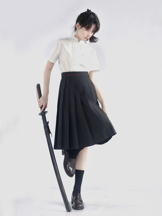 a young woman stands in a studio setting, posing with a katana sword. she wears a stylish, minimalist outfit consisting of a white, shortsleeved blouse and a black pleated midi skirt. the image is welllit, providing a clean and modern aesthetic. her black shoes and the red accent on the sword subtly complement the monochrome color scheme.