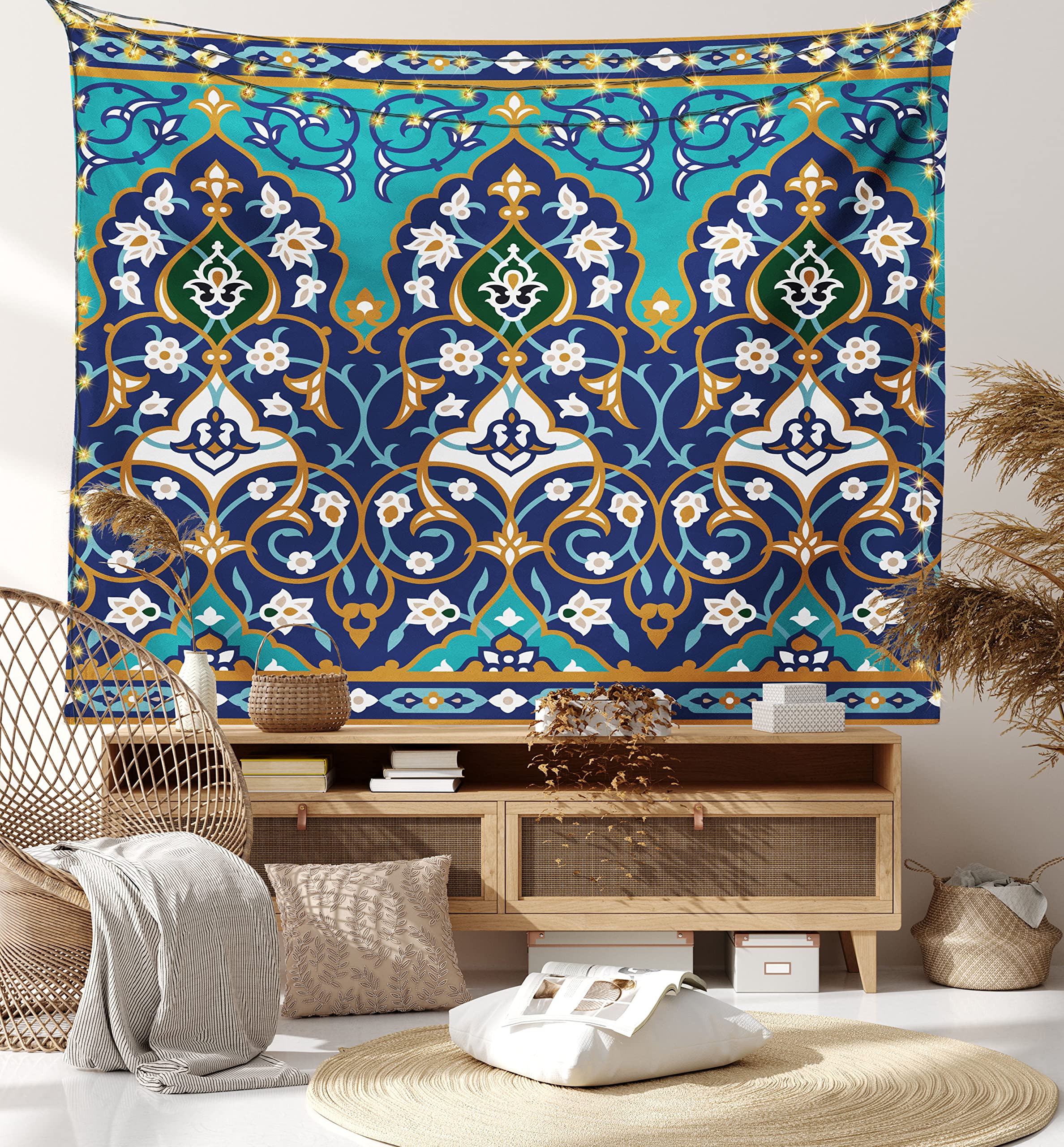a room interior is decorated with a tapestry. the tapestry, featuring an oriental floral pattern in blue, turquoise, gold, white, and green, hangs behind a light woodcolored cabinet. in front of the cabinet is a wicker chair with a cushion, a throw pillow, a round rug, and assorted decorative items.