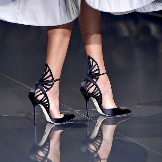 a woman in a black and white dress with a black skirt and a black top, showing off her legs in a pair of black high heels, with a lace pattern on the top. she has a confident pose, which gives off a sense of style and elegance. her high heels add a touch of glamour and style to her look.