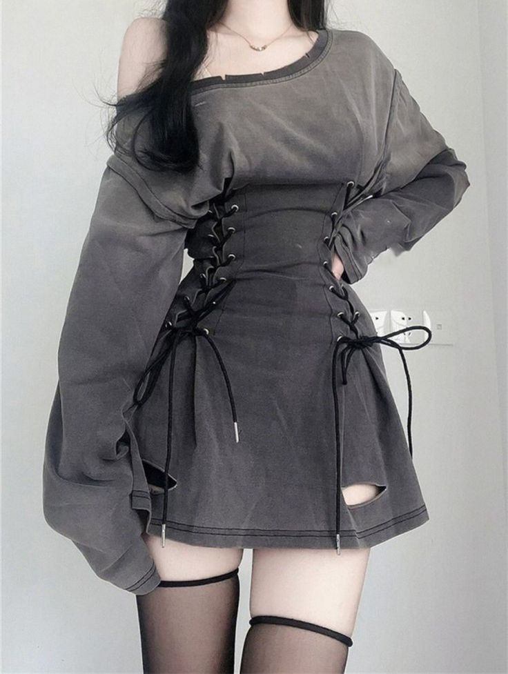 a young woman in a stylish grey  outfit poses for a photo. she is wearing a grey shirt with a black lace up corset and a grey skirt that has a slit in the front.  her long black hair falls around her shoulders.  the outfit is a stylish and edgy look.