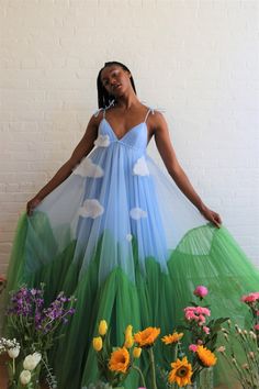 a young woman in a beautiful blue and green tulle dress.  the dress has white cloud shapes sewn onto the bodice, and the bottom of the dress has a green  tulle gradient to represent grass.  she stands in a field of flowers with a bright and dreamy look.