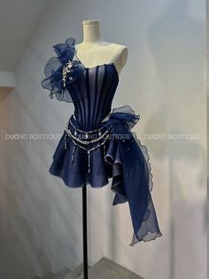 a navy blue evening dress with corset bodice, tulle skirt, silver beading and floral detail on shoulder is displayed on a mannequin in what looks like a boutique showroom.