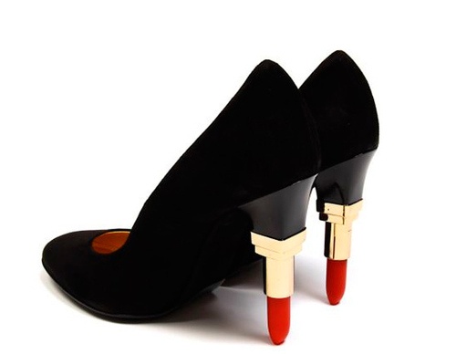 a closeup shot of a pair of black high heels with unique lipstickshaped heels. the heels are made of black suede and have a goldcolored base that resembles a lipstick tube with a red lipstick bullet at the bottom. the shoes are angled slightly, and the focus is on the detail of the lipstick heels. the background is simple white, emphasizing the shoes.