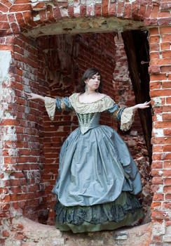 a woman in a long, elegant blue and green period dress stands in a crumbling brick archway. the dress is richly detailed with ruffles and layers. the setting appears to be the ruins of an old building. the overall style suggests a historical or period setting, possibly 18th or 19th century. the woman's pose is graceful and slightly melancholic. the contrast between her elegant attire and the dilapidated backdrop creates a compelling visual.