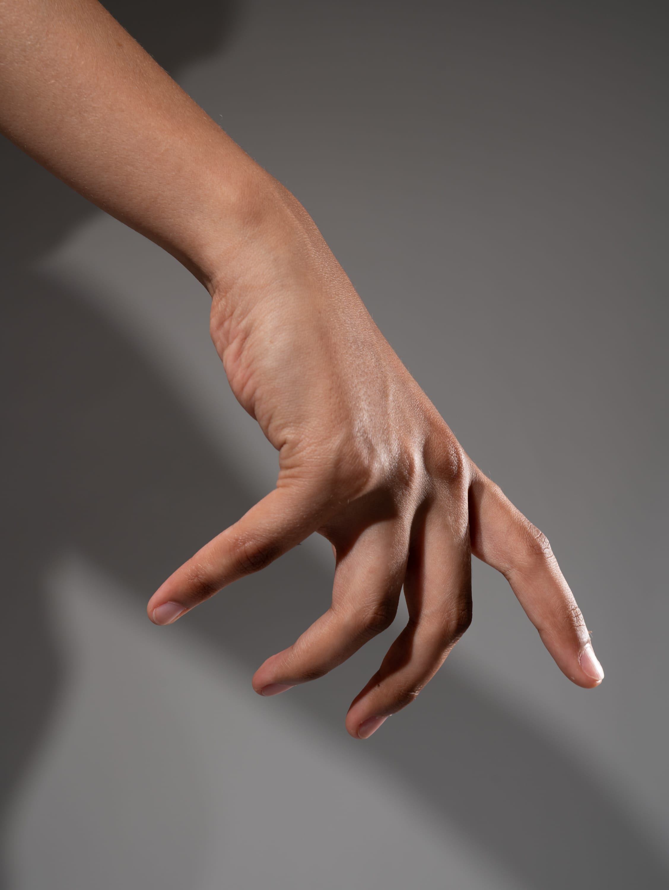 a hand is reaching out as if to grab something. the hand is illuminated by studio lighting which casts a shadow on the background. the hand appears to be that of a person with light brown skin.