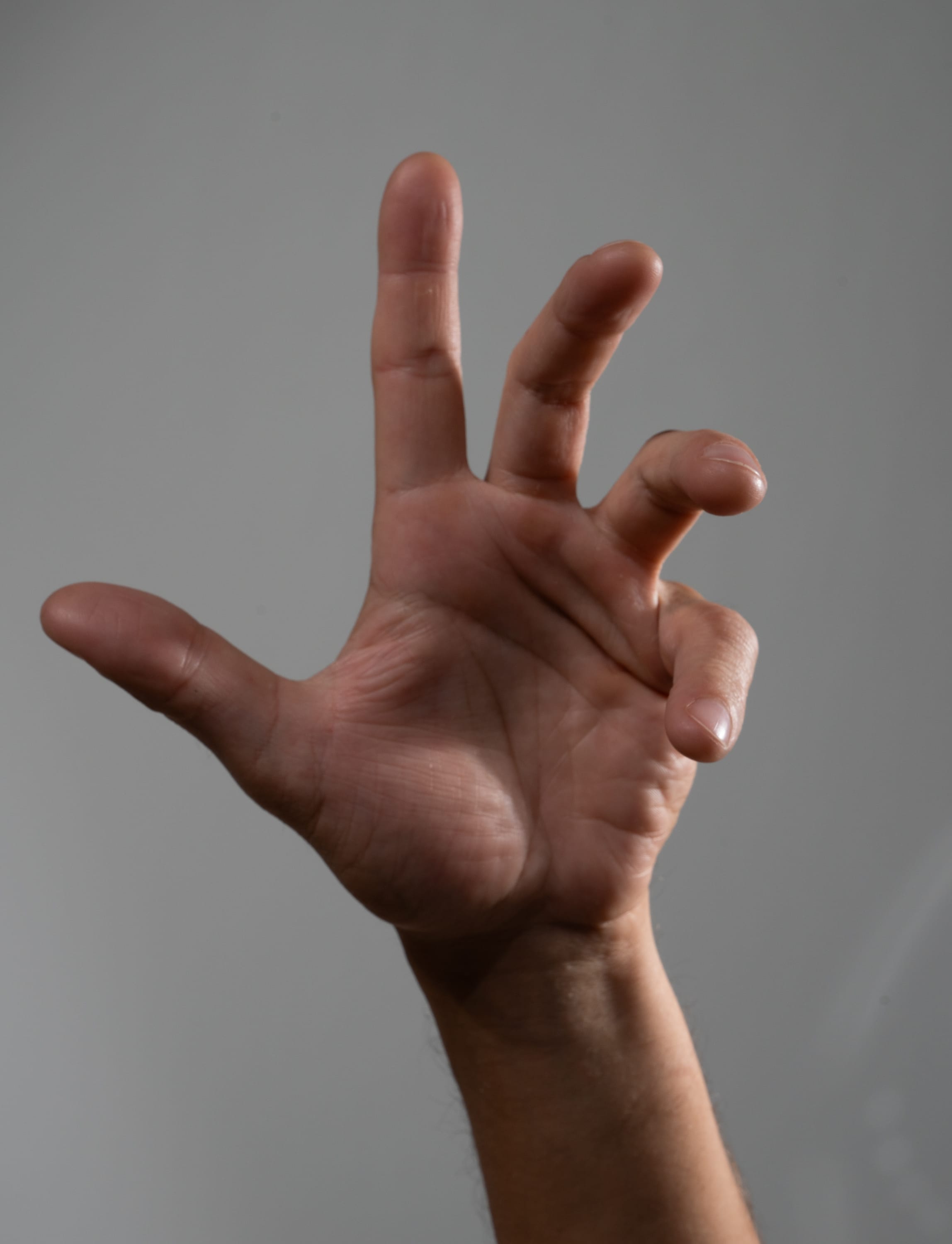 a closeup image of a hand with its fingers spread out in a clawlike gesture against a plain grey background. the image is taken from a low perspective, making the hand appear larger and more imposing.