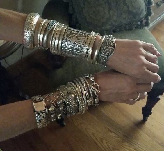 a woman's arms are adorned with many silver and gold bracelets, bangles and other jewelry.  the bracelets are elaborate and intricate, some of them appear to be antique. the image is a close up of the woman's arms and hands.