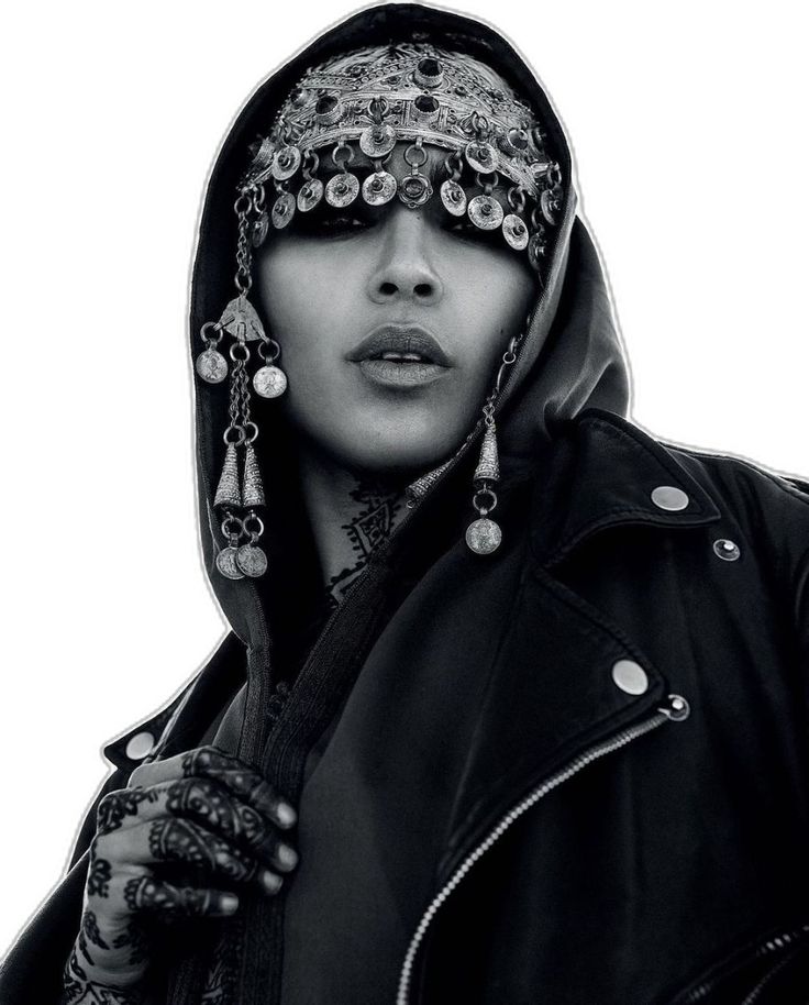a black and white portrait of a woman wearing a black leather jacket and a head scarf with silver jewelry. she is looking directly at the camera with a serious expression. her hand is resting on her jacket. the image is lit in a way that highlights her features and the details of her outfit. the background is blurred, suggesting a studio setting.