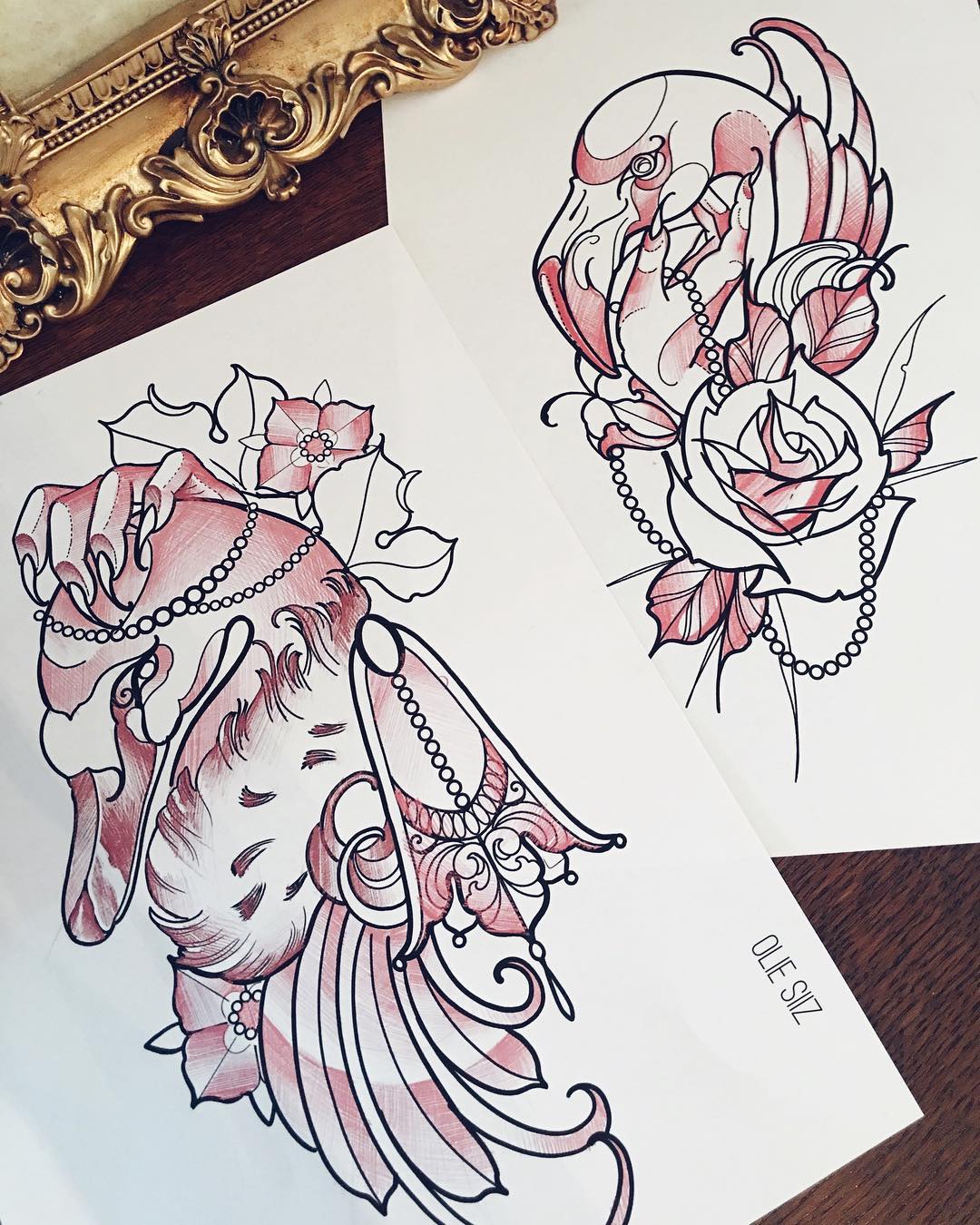 this image shows two tattoo design sketches on white paper. the drawings are of birds, one flamingo and one swan, surrounded by flowers, chains, and jewelry. the drawings are outlined in black and shaded with red ink.  the artist's signature "ole siz." is visible in the bottom right corner. there's a gold picture frame partially visible in the background.