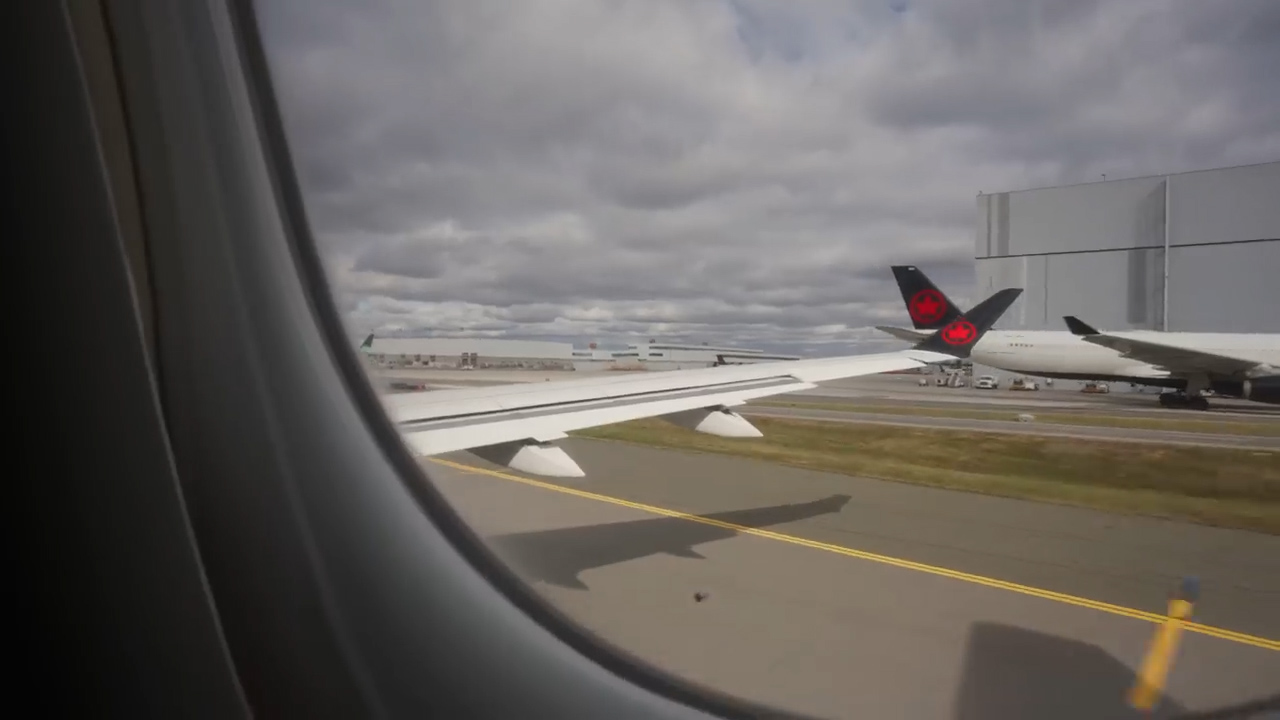 this is a view from the window of an airplane that is preparing for takeoff. you can see the wing of the airplane, the tarmac, and another airplane in the background. the sky is cloudy.
