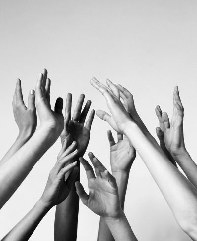 a black and white photo of multiple hands reaching up with their fingers extended as if they are reaching for something. the photo is taken from a low angle looking up at the hands.