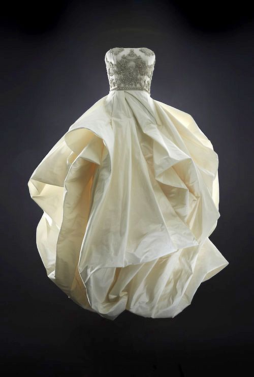 a stunning white wedding dress with a strapless bodice adorned with intricate beading and lace. the skirt is voluminous and features dramatic ruffles, creating a grand and elegant silhouette. the dress is made of luxurious silk and is perfect for a special occasion like a wedding ceremony.
