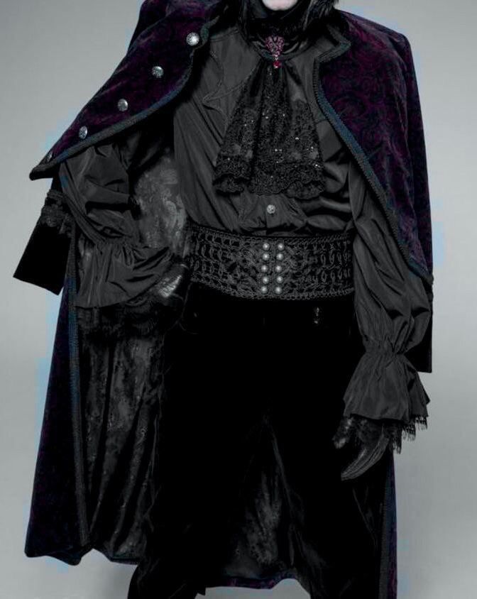 a person wearing a gothicinspired ensemble. the outfit features a dark velvet cloak with ornamental buttons, a black blouse with lace detailing around the collar, a decorative belt with silver accents, and ruffled sleeves. the overall aesthetic is reminiscent of a vampire or dark victorian style.