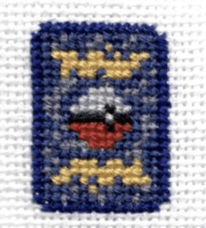 a closeup shot of a crossstitch piece. the image is of a blue square with a red, white, and yellow design inside. the square is surrounded by a white background.  the detail of the cross stitch is very clear.