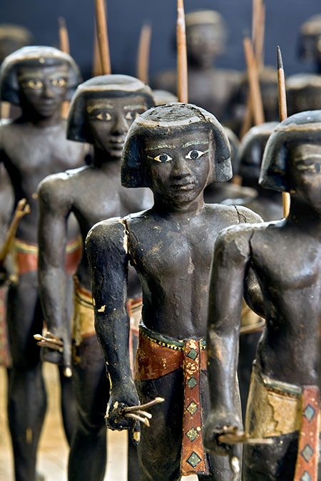 a closeup view of a row of wooden figurines depicting ancient egyptian soldiers. the figurines are dark brown with painted details, holding spears and wearing loincloths. they stand in formation, showcasing the artistry and craftsmanship of ancient egypt.