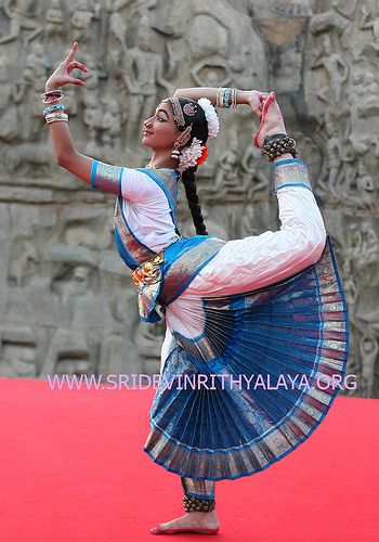 a young woman, dressed in traditional indian attire, performs a graceful dance pose. she is wearing a bright blue and white saree, with intricate jewelry and a flower adorning her hair. she appears to be in a state of concentration and her movements convey a sense of artistry and elegance.  the image captures the beauty and richness of indian culture.