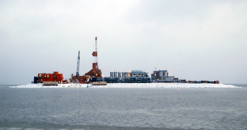 a large oil rig is situated on a small island in the middle of a frozen sea. the rig is surrounded by snow and ice, and the sky is overcast. the drilling platform and equipment are visible in the center of the island. there are numerous buildings and facilities on the island that are connected to the drilling platform. this oil rig is likely located in the arctic, where oil exploration and production is increasingly common. the image captures the harsh and remote environment of the arctic and the challenges associated with oil extraction in these extreme conditions.