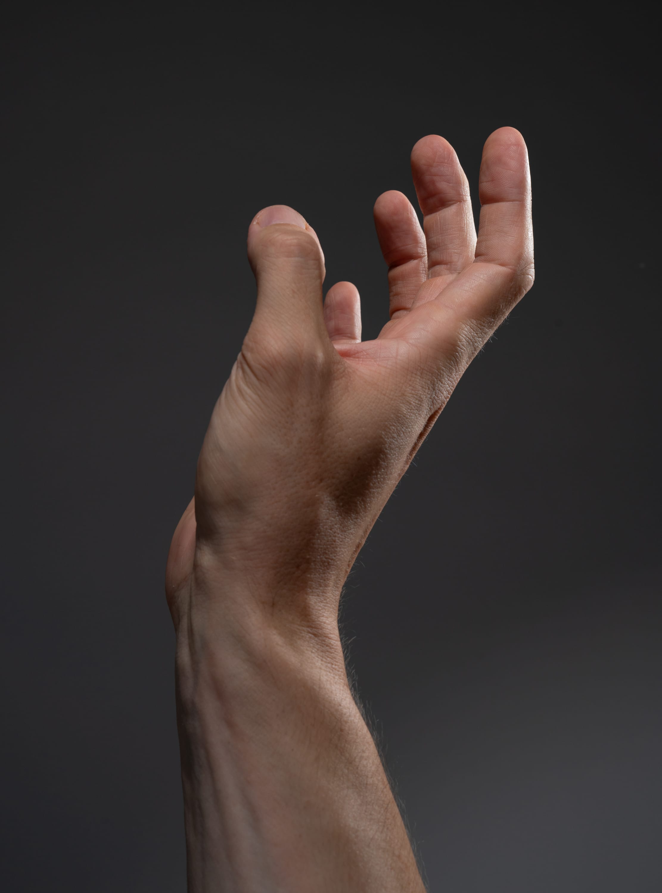 a male hand is reaching up with slightly spread fingers against a gray background. the image is shot from a low perspective, creating a sense of aspiration or longing.