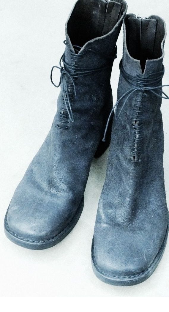 a pair of dark suede laceup ankle boots are positioned on a white surface. the boots feature a rounded toe and a short heel. the laces are tied around the ankles.