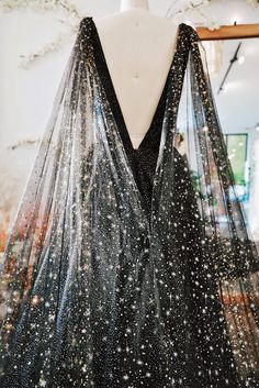 a black tulle dress with glitter stars is shown in a closeup. the dress is sheer and sparkly, and the glitter stars are scattered throughout the tulle. the dress has a plunging vneckline and a long, flowing skirt. it is perfect for a special occasion, such as a wedding or prom.