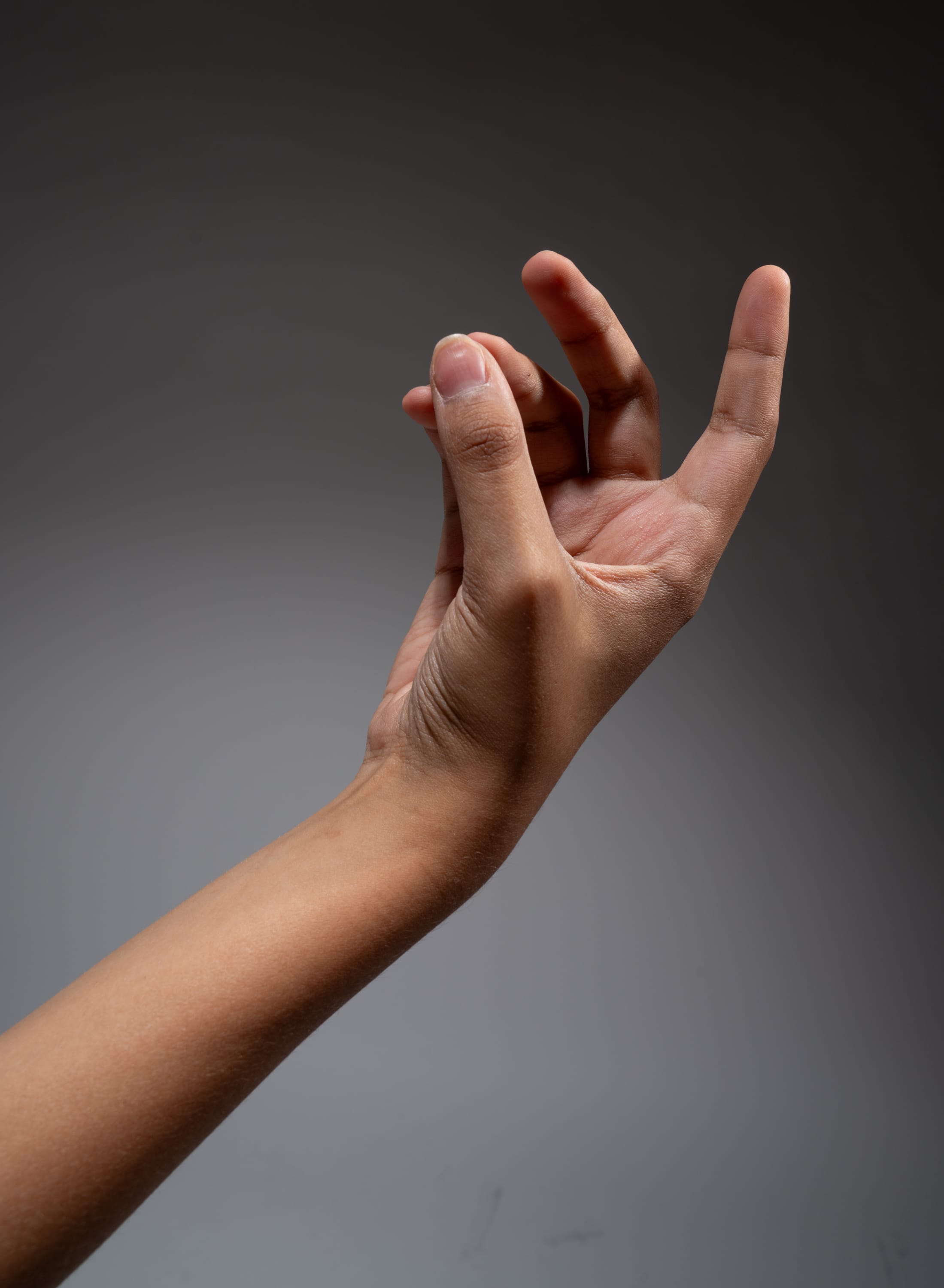 a hand is reaching out with the thumb and index finger slightly pinched together. the hand is positioned against a grey background. the hand appears to be reaching out to pick up or grasp something small.