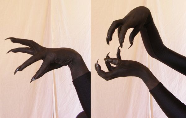 two hands wearing black gloves with long, sharp claws. the hands are posed against a white background.