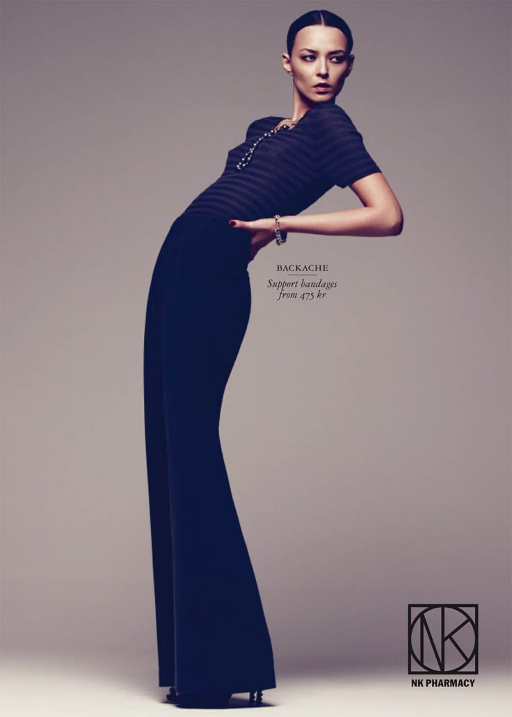 a female model is leaning backward in a dramatic pose, wearing a black striped top and widelegged black pants. she has dark hair slicked back and is wearing jewelry. the image is an advertisement for "backache support bandages from 475 kr" with the "nk pharmacy" logo in the lower right corner. the background is a neutral grey.
