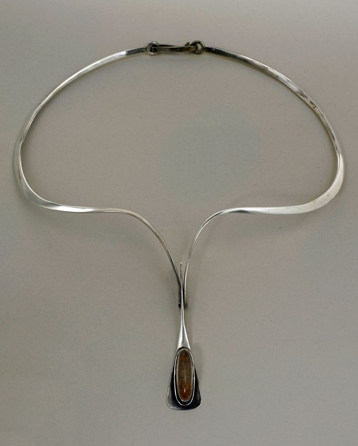 a closeup overhead shot of a silver necklace with a minimalist design. the necklace has a smooth, curved collar that splits into a yshape, ending in a pendant with an oval sunstone. the overall style is modern and geometric, possibly midcentury modern or scandinavian in influence. the necklace is displayed against a light gray background.