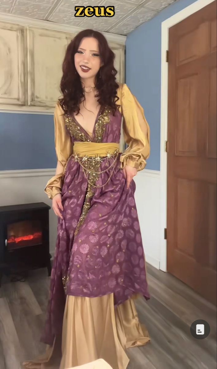 the image shows a young woman in a zeus costume indoors. she is dressed in a purple and gold gown with puffed sleeves and a gold belt. the text "zeus" is written above her head.