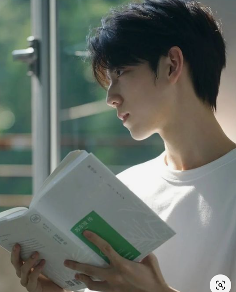 a young man is shown in profile, engrossed in a book. the scene is bathed in natural light streaming in from a window, creating a sense of calm and serenity.  the man's expression suggests deep thought and concentration as he absorbs the contents of the book.