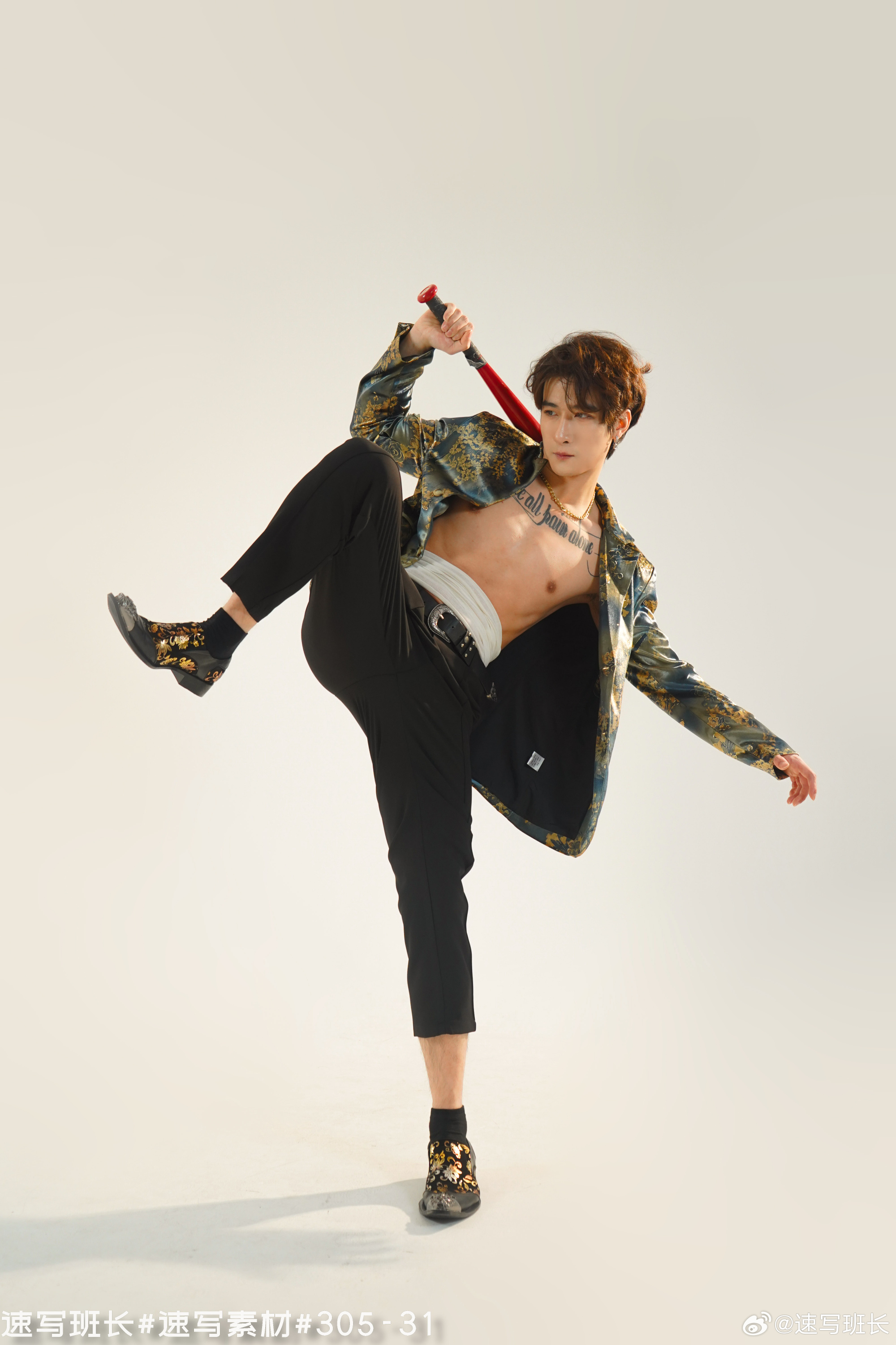 a young asian man in a stylish outfit is striking a dynamic pose in a studio setting. he's wearing a partially unbuttoned brocade jacket, black pants, and unique shoes. his torso is bare, showcasing tattoos. he's holding a red baseball bat above his head, adding to the edgy and powerful vibe. the image is welllit, highlighting the details of his clothing and physique.
