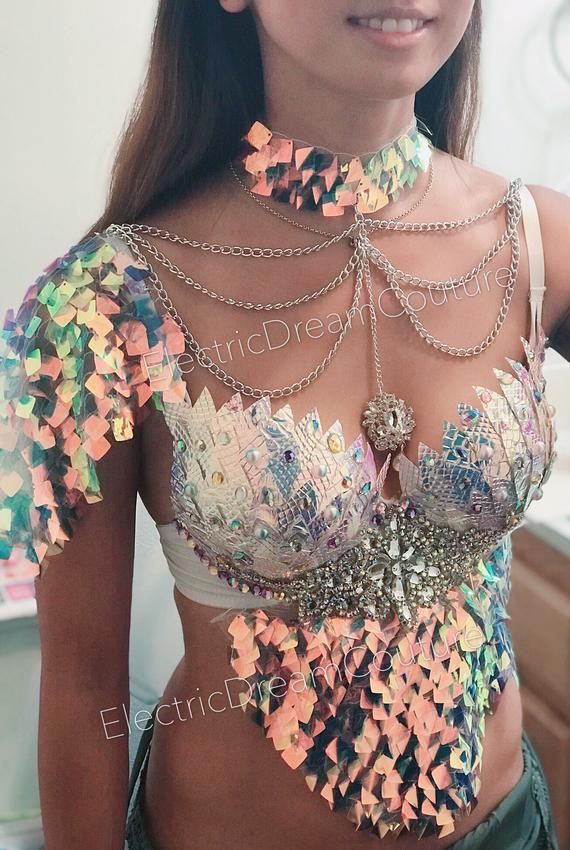 a woman is wearing a sequin and chain rave outfit that consists of a bra, choker, and shoulder covering. the pieces are iridescent and colorful.