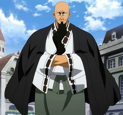 the image shows an anime character, a male, with a black beard and hair. he is bald and has dark eyes. he is wearing a black and white long sleeve outfit. he is standing in front of a building. the background is a blue sky with white clouds.