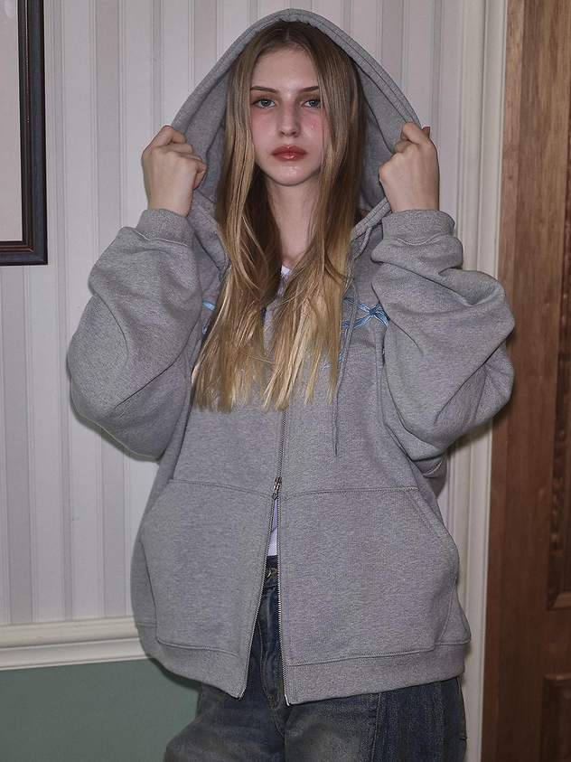 a woman with blond hair is wearing a gray hoodie and jeans. she is standing indoors.