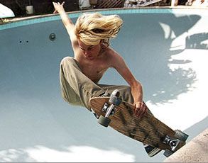 a young skateboarder does an aerial trick over a pool. he is wearing brown pants and has blond hair.