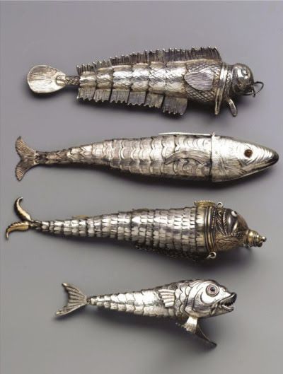 the image contains four silver antique fish sculptures/decorations. they vary in design and appearance. some have detailed scale patterns, while others have more abstract designs. they appear to be collectibles or antique tableware/utensils.