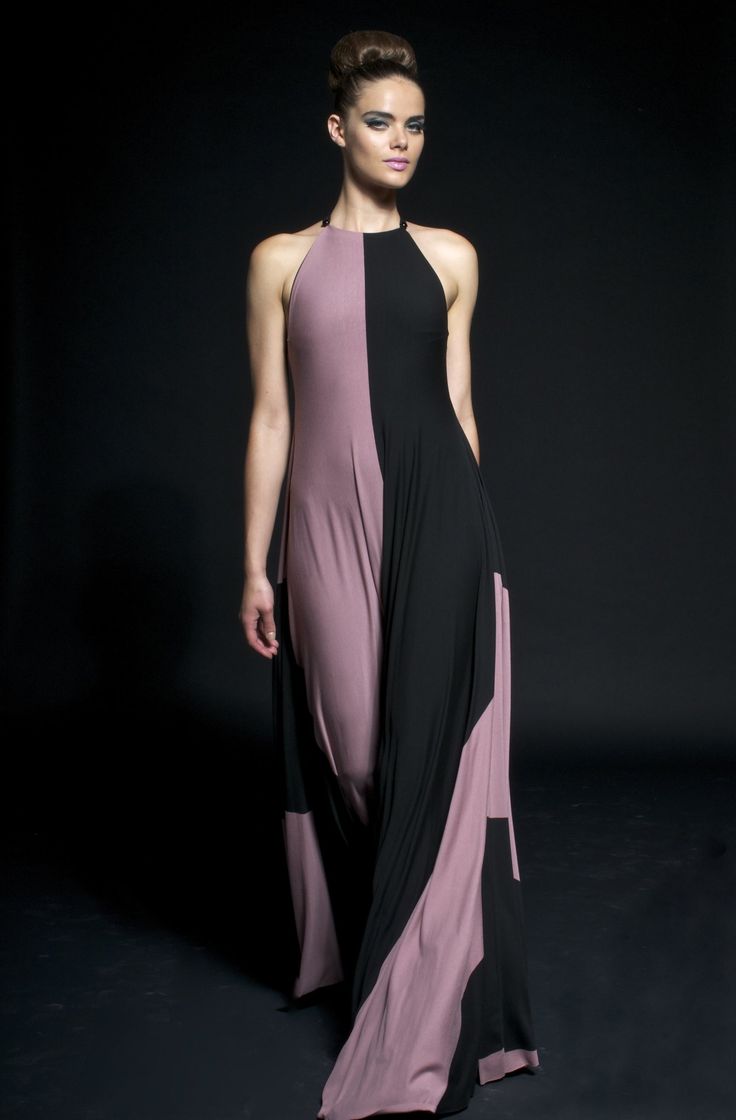 a woman model is wearing a purple and black dress, posing on a runway in a studio. she is wearing a halter neck dress with a black stripe going down the middle and the sides. the dress is flowing and elegant. she looks glamorous and stylish.