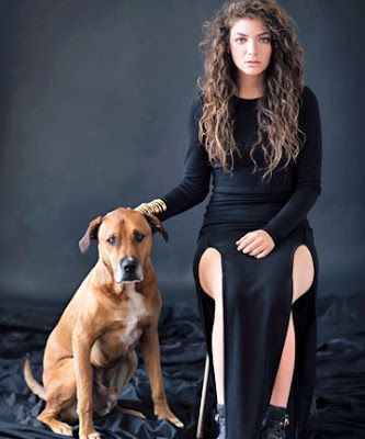 a woman is sitting on a black background and posing with her dog. the woman is wearing a black dress, and the dog is brown.