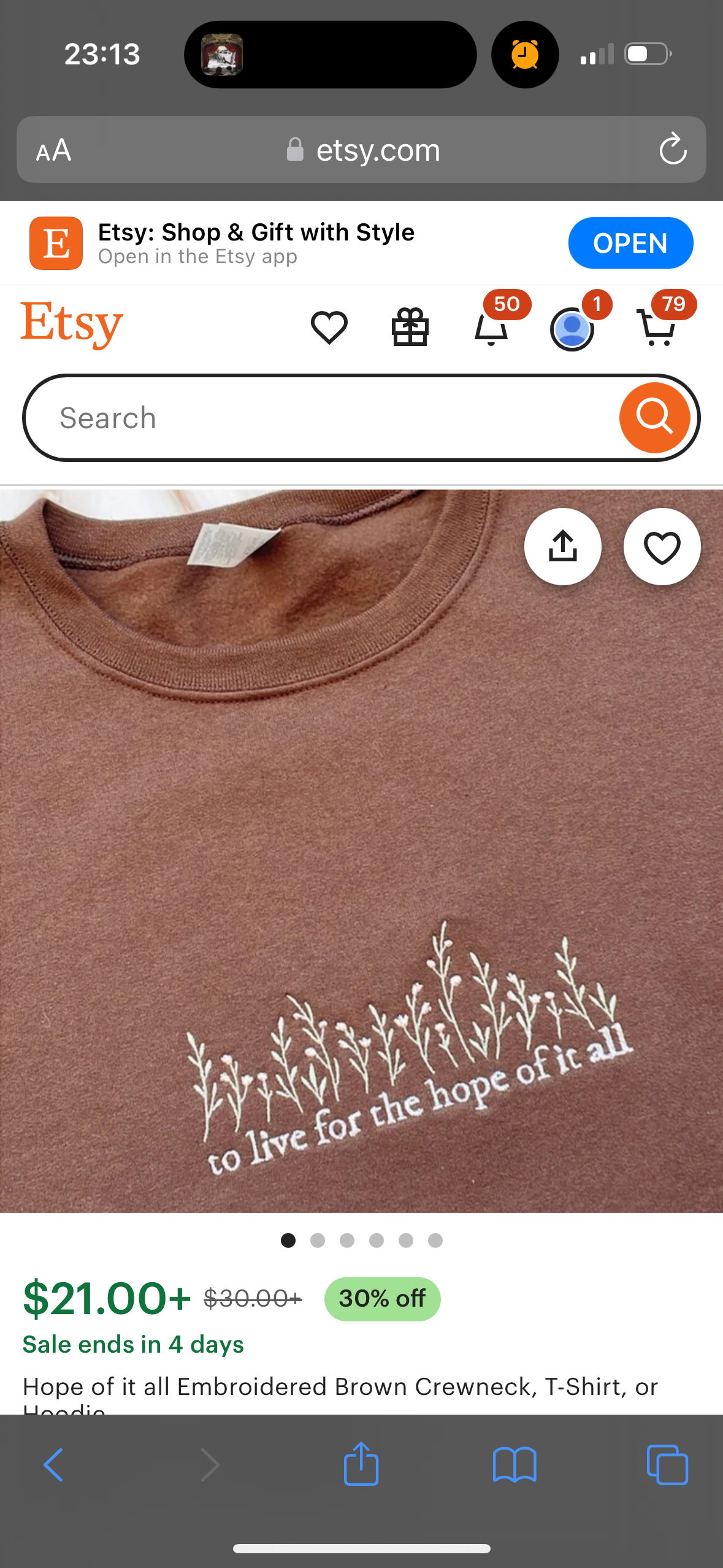 this image is a screenshot of an etsy product page. the item is a brown crewneck tshirt with white embroidered floral design and the text "to live for the hope of it all". the product is on sale, and the original price, sale price, and discount percentage are displayed. there is a button to open the etsy app.  the etsy logo is visible at the top of the screen. the image is taken from a smartphone and shows the typical layout of a product page on etsy.