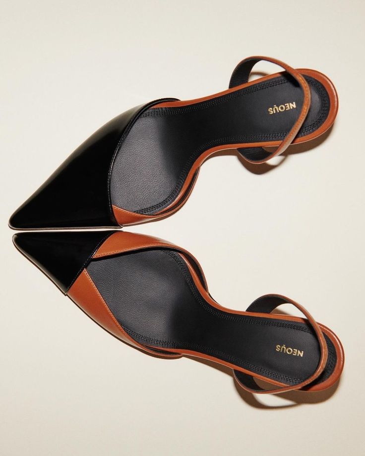 a highangle, full shot depicts a pair of neous slingback heels. the shoes are twotoned, with black patent leather on the toe and brown leather on the heel and vamp. the shoes are arranged with one shoe on top of the other, slightly overlapping.  the background is a light beige.  the neous branding is visible on the insole of both shoes.