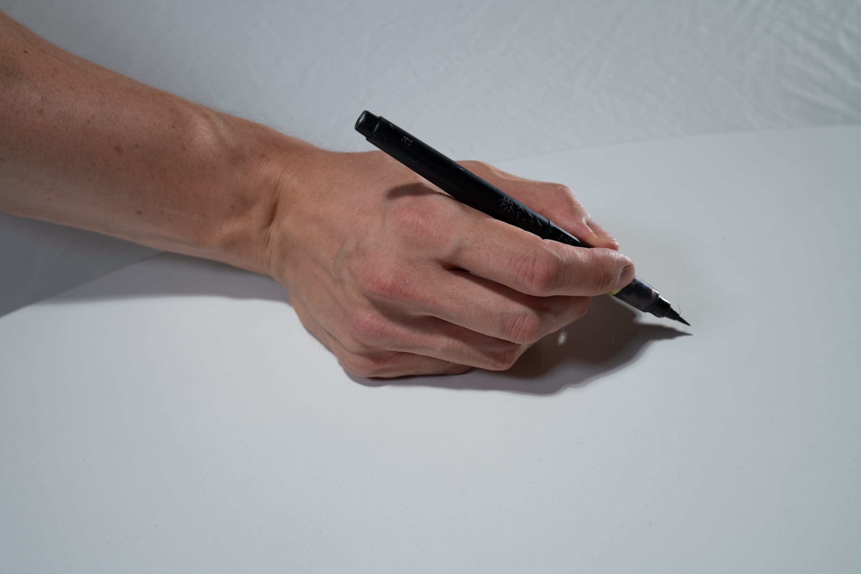 a hand is holding a black pen on a white surface.