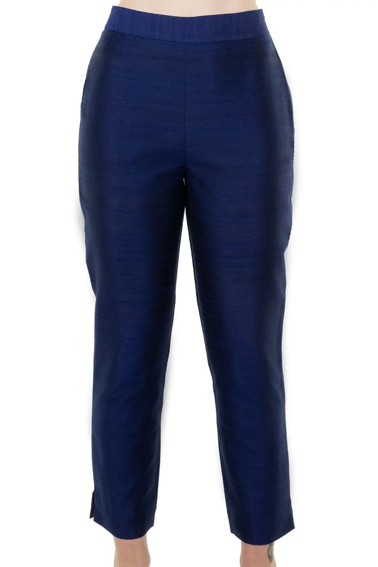 a close up image of a woman's dark blue slim fit ankle length pants. the pants are made from silk. the woman is wearing a white shirt.