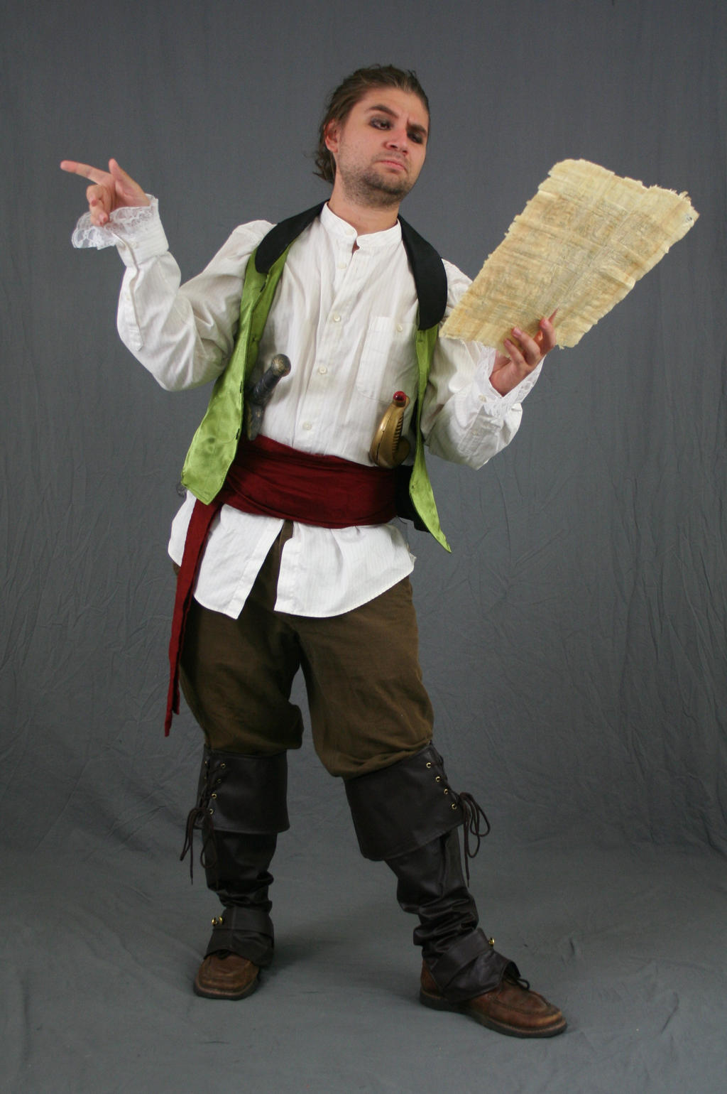 a full shot of a man dressed in a pirate costume. he's wearing a white shirt, a green vest, brown breeches, dark boots, a red sash, and accessories like a dagger and flask. he's holding and looking at a piece of parchment, and gesturing with his other hand. the background is a plain gray studio backdrop.  the overall style suggests a historical or theatrical setting.